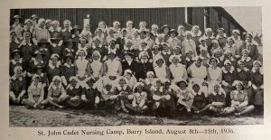 A black and white photograph of a large group of Nursing Cadets, sitting, kneeling, and standing for a group photograph. They are smiling, and some are wearing large sunhats.