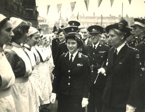 Black and white photograph showing Princess Margaret in St John uniform inspecting a row of Nursing members outdoors, St John dignitaries following behind