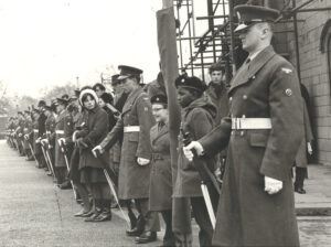 A black and white photograph showing two male St John Ambulance Cadets standing in front of crowds lining the route at Winston Churchill&apos;s funeral. The Cadets appear to be standing in line alongside men wearing RAF uniforms.