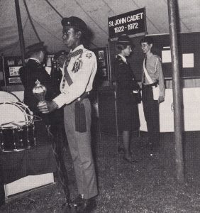 Princess Anne, accompanied by uniformed adult members of St John Ambulance, is talking to a male Cadet about the display behind him. In the foreground is another male Cadet standing as Princess Anne's guard of honour.