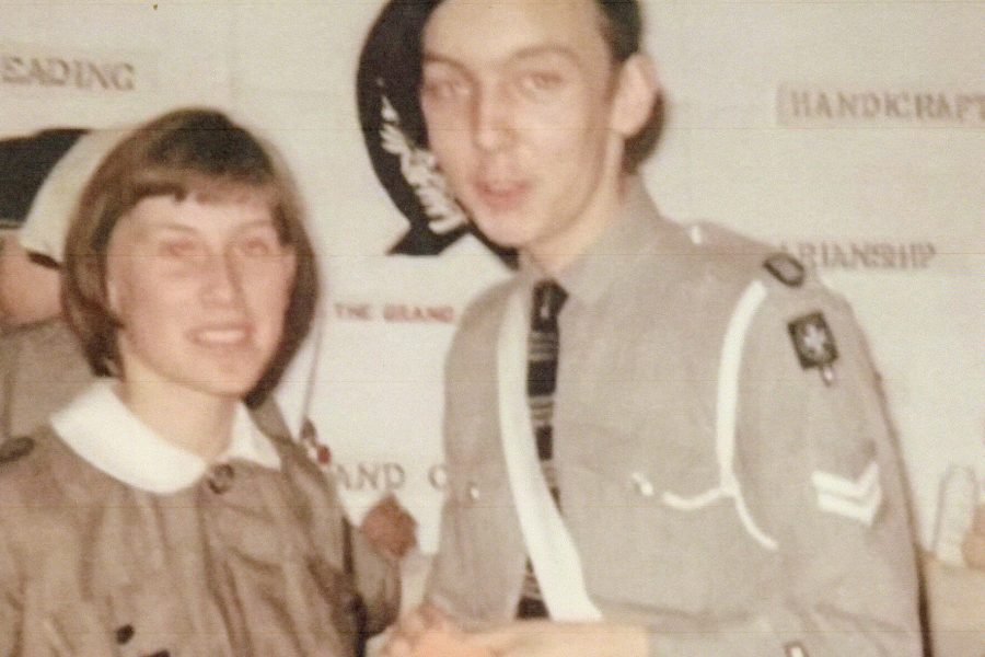 A faded photograph with a white Nursing Cadet on the left wearing a grey knee length dress with a white collar belted at the waist. The dress has a pocket on the chest with a black badge bearing St John’s 8 pointed cross. She is also wearing a white nursing cap towards the back of her head. To the right of the photo is a white male Cadet wearing a black beret