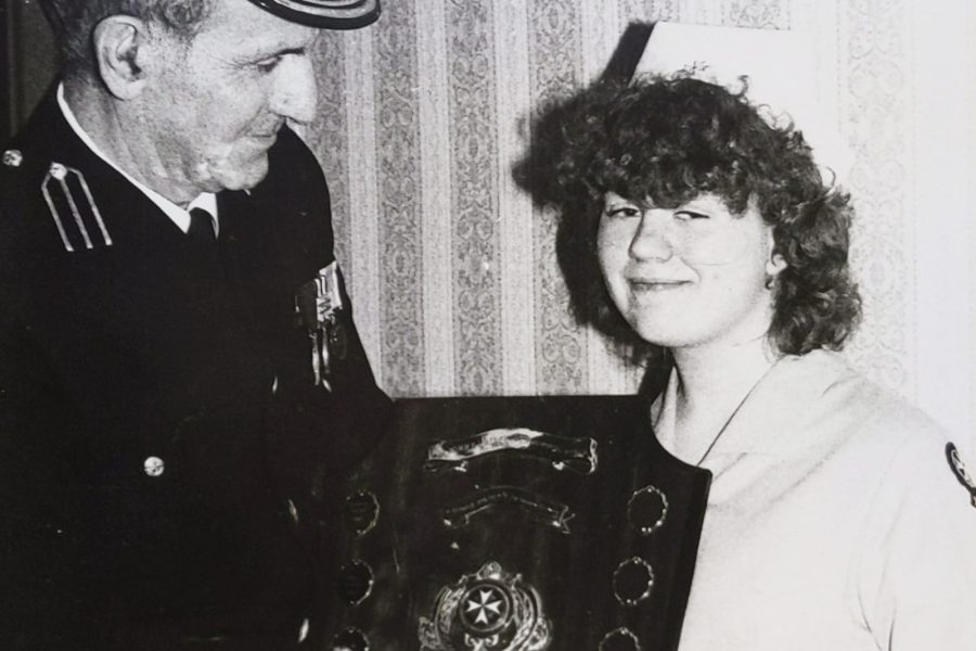 Black and white image of a young female in St John Ambulance uniform standing to the right of an adult male in uniform. The adult is presenting the girl with a large trophy.