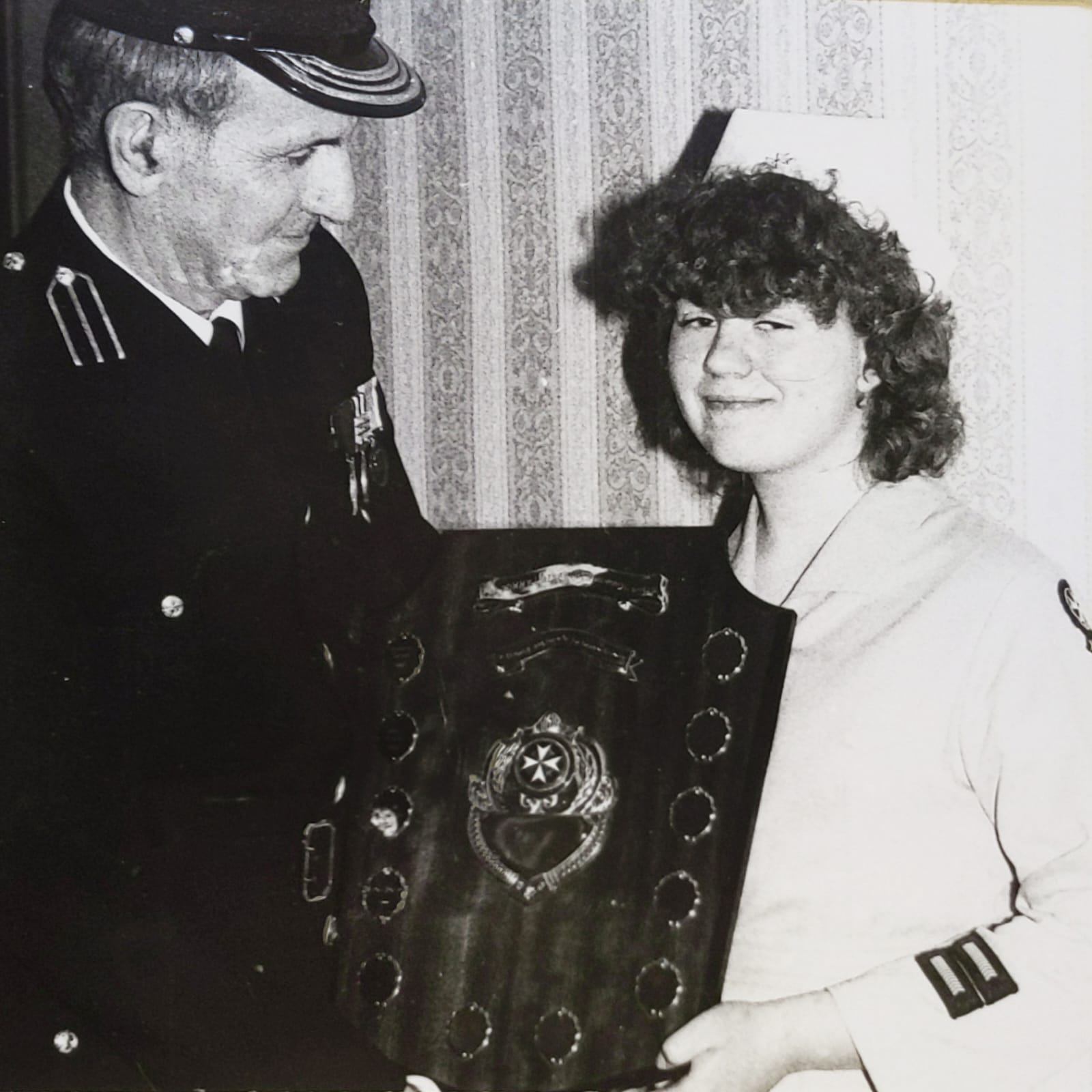 Black and white image of a young female in St John Ambulance uniform standing to the right of an adult male in uniform. The adult is presenting the girl with a large trophy.