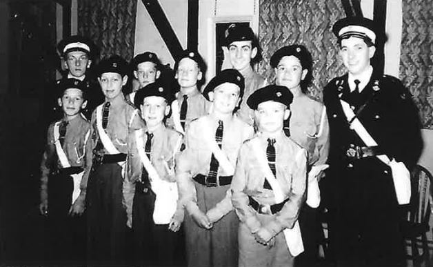 Black and white photograph of nine boy Cadets and two adults standing in uniform.