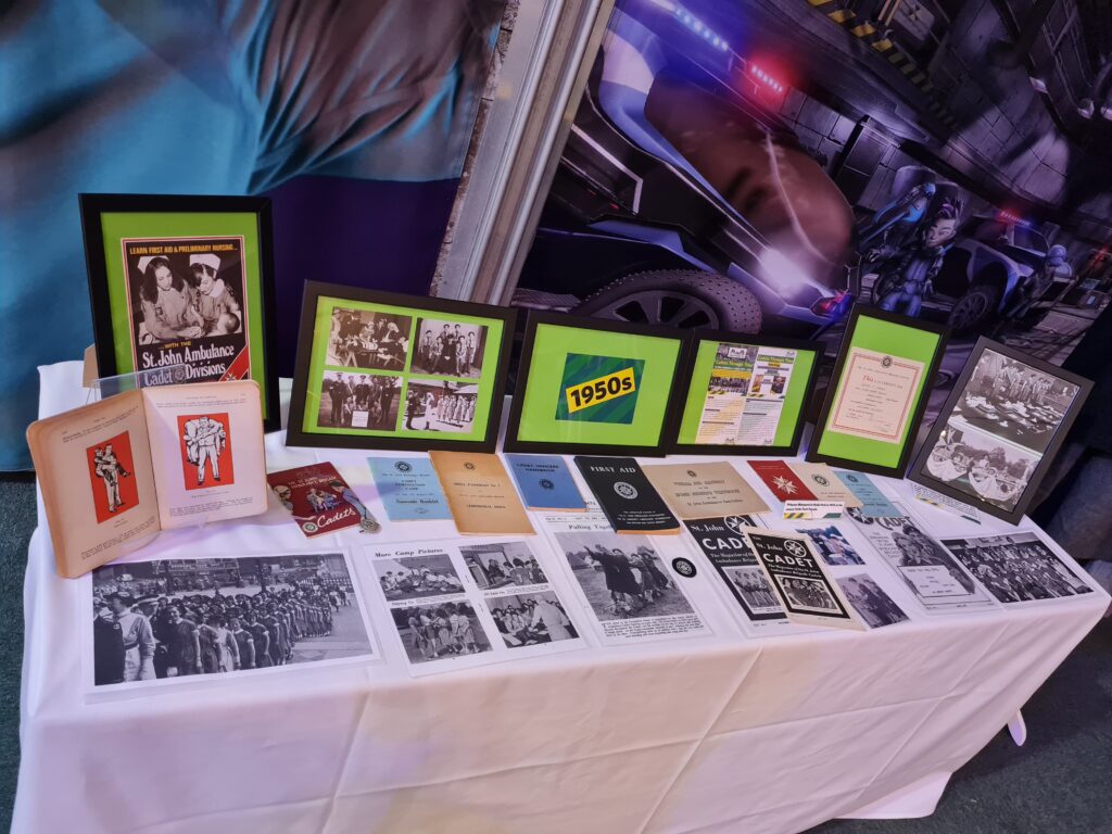 Colour photograph of a table covered with old photographs, magazines and booklets on a white tablecloth illustrating Cadet activities in the 1950s.