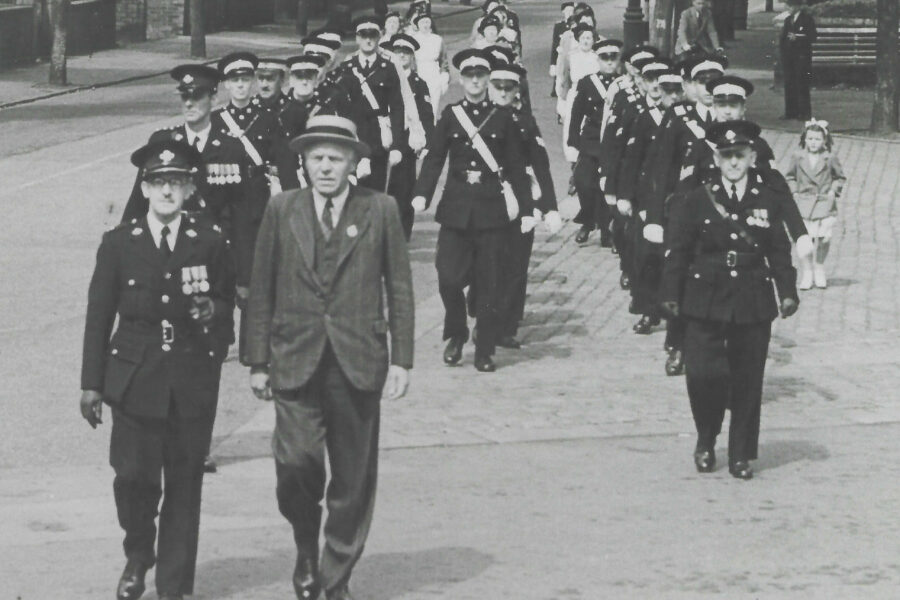 Black and white images of three rows of men in uniform who are walking in the direction of the photographer.  Behind them are three rows of nurses in uniform
