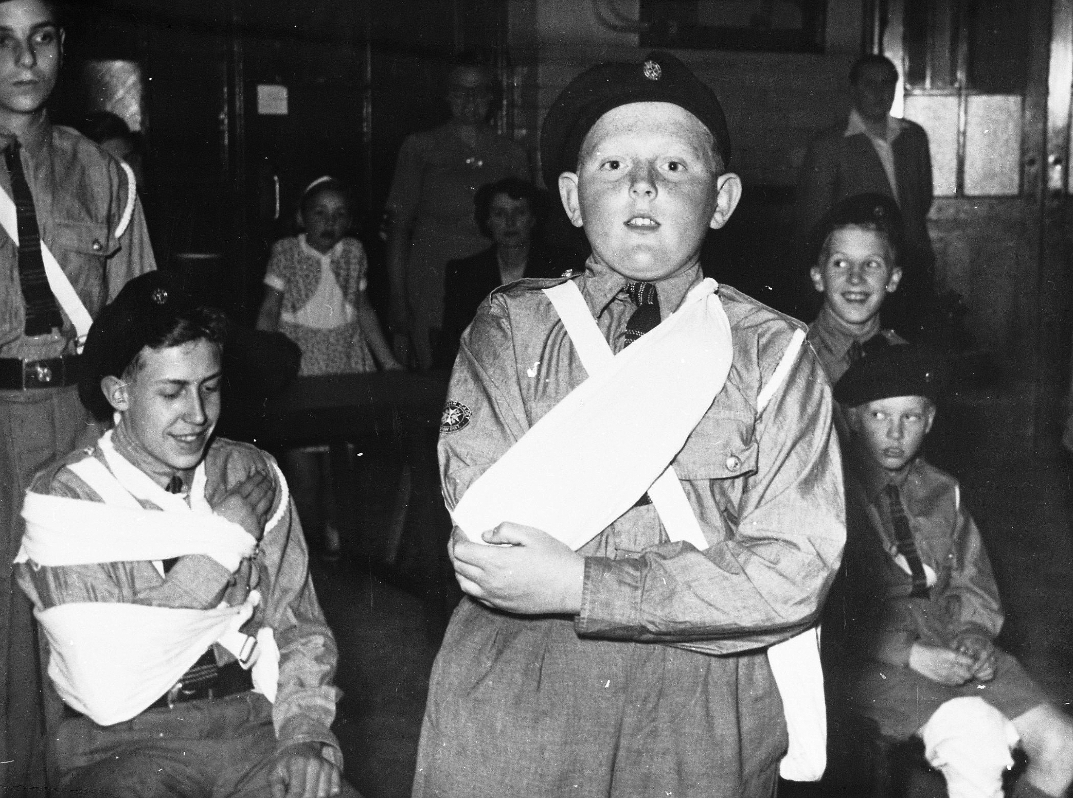Black and white photograph of a young boy in uniform with his arm in a sling. Beside him to the left is a girl