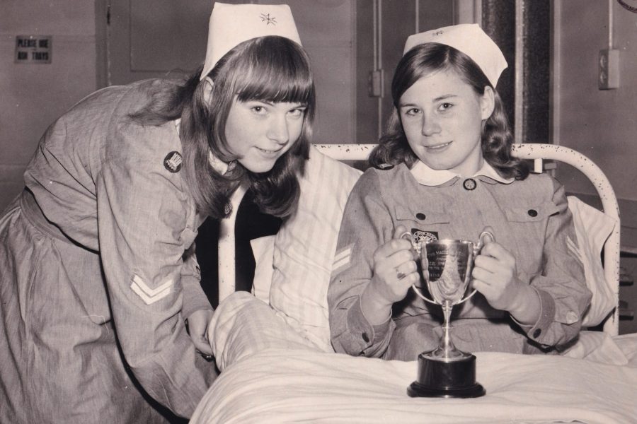 Black and white photograph of two young women wearing nursing uniforms consisting of long sleeve dresses and white hats. One of the girls
