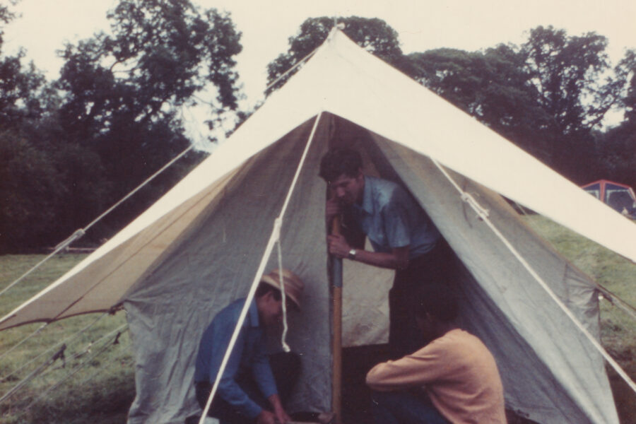 Colour photograph of three boys erecting a tent in a field.
