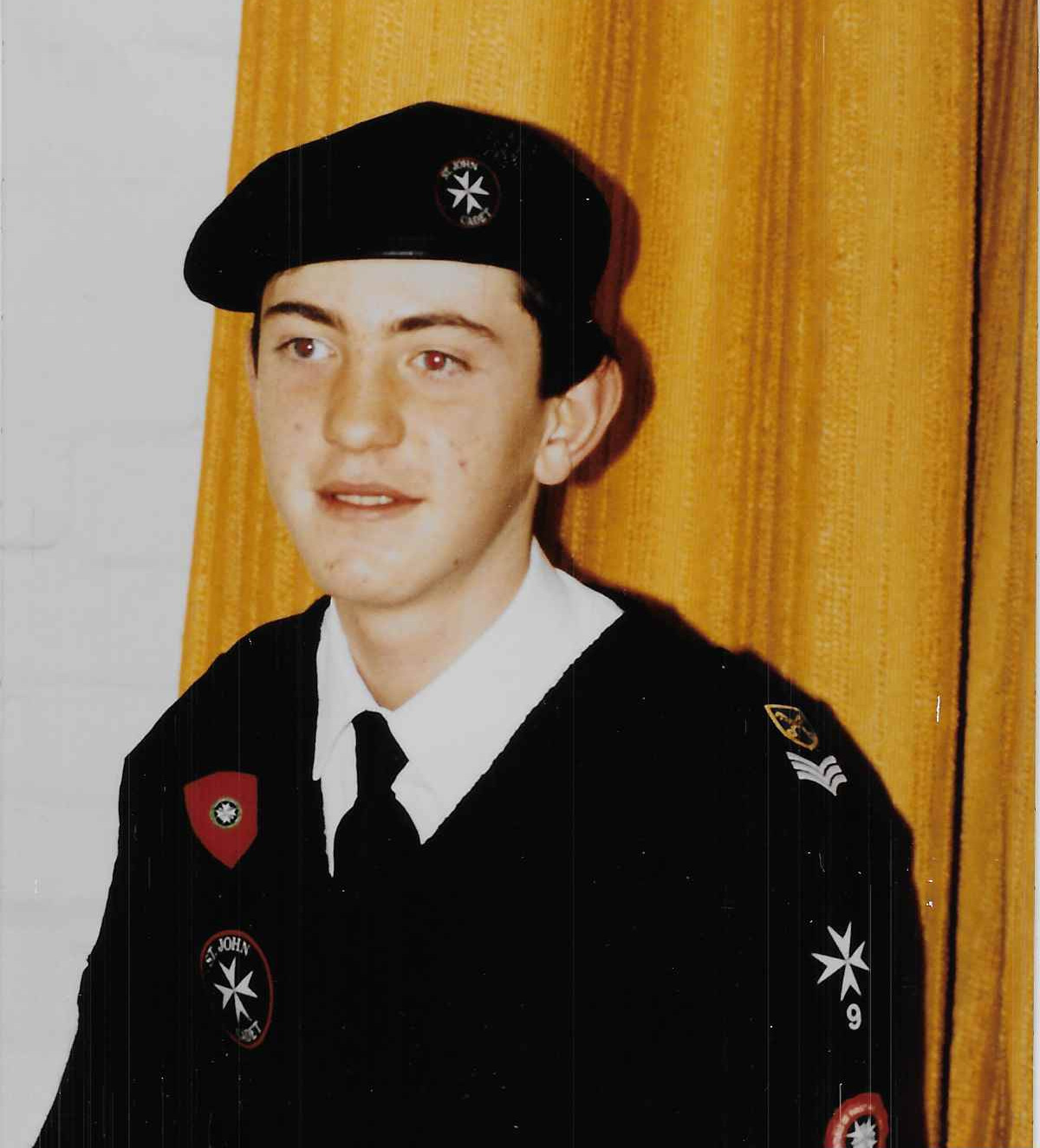 Colour photograph showing a young male Cadet in uniform. He is smiling and looking slightly off camera. He wears a white shirt