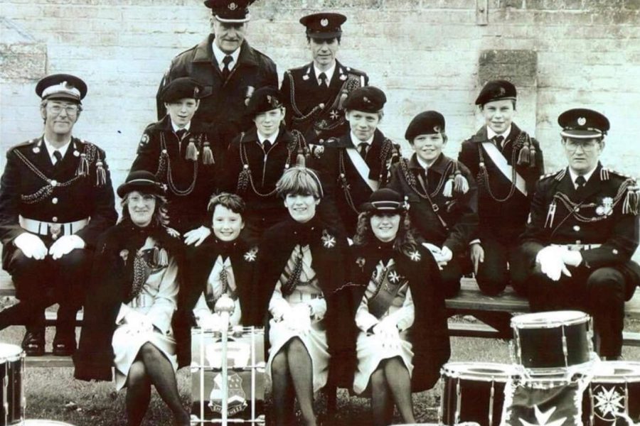 Black and white group photograph of adult and Cadet members of Isle of Sheppey division, seated outside. Drums and other musical instruments are laid out on the ground in front of them.