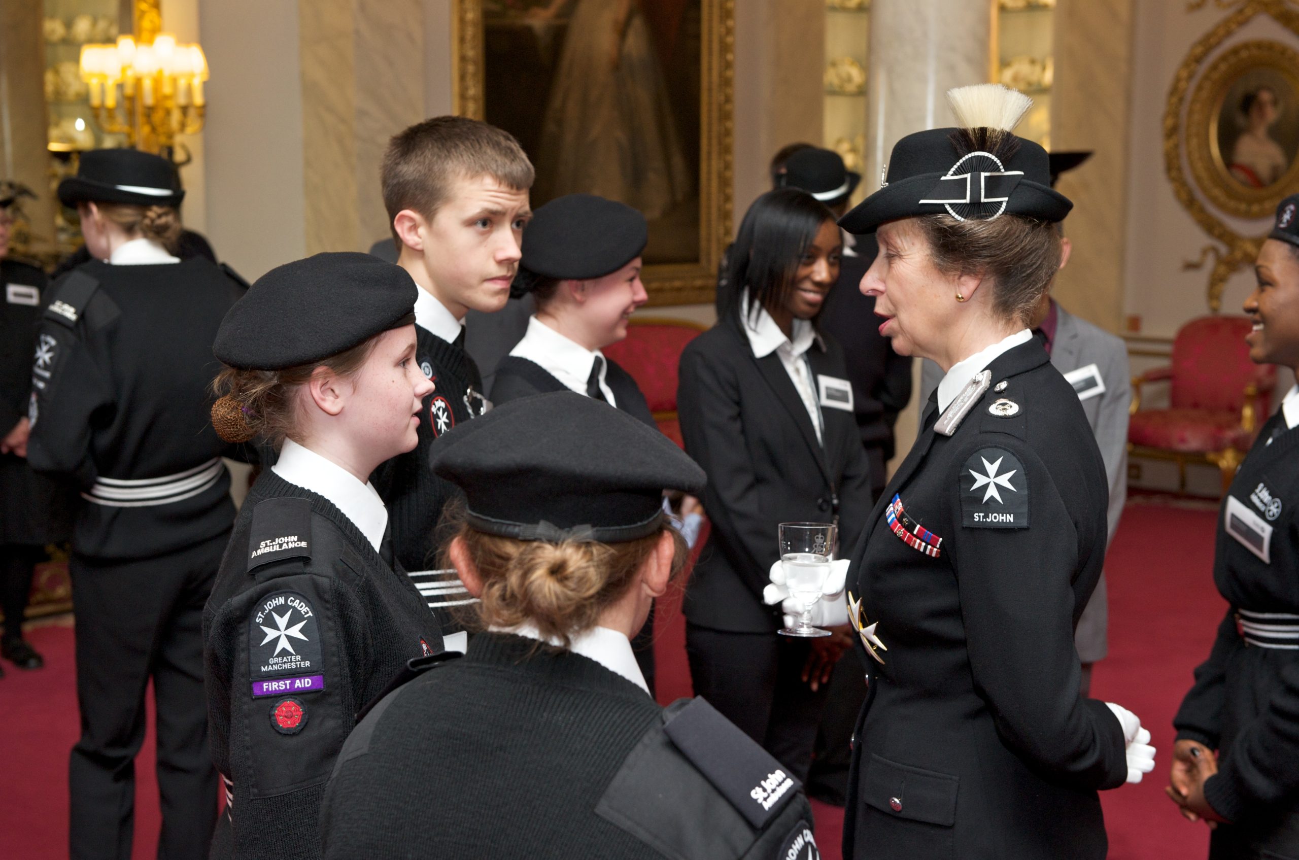 Group of Cadets in black and white St John uniform stand as they meet Princess Anne, also wearing St John uniform.