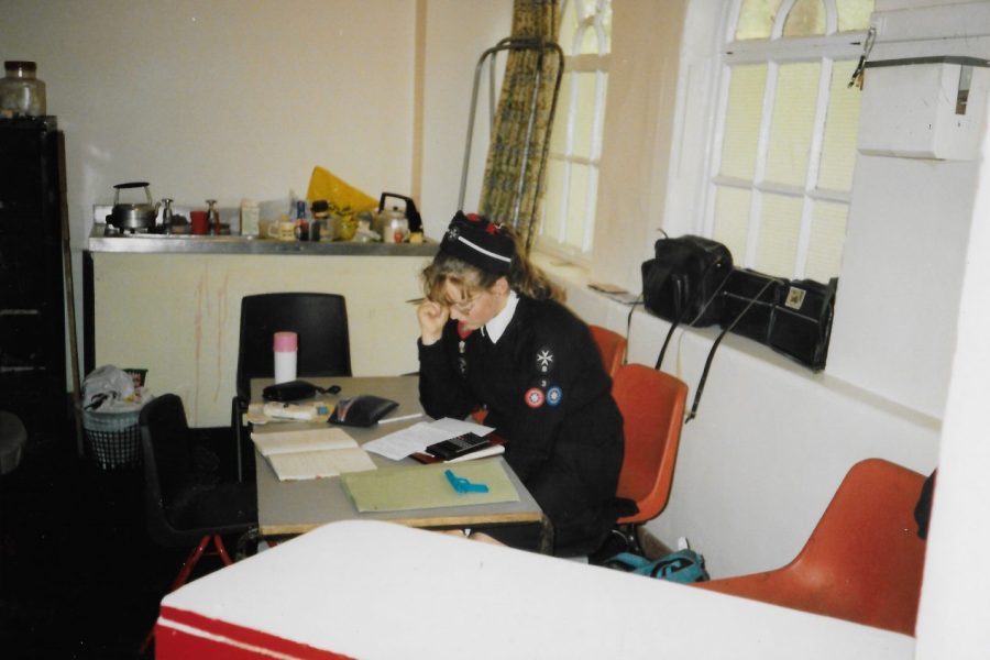 Colour photograph of a Cadet in black and whute uniform seated at a table in a kitchen, studying notes