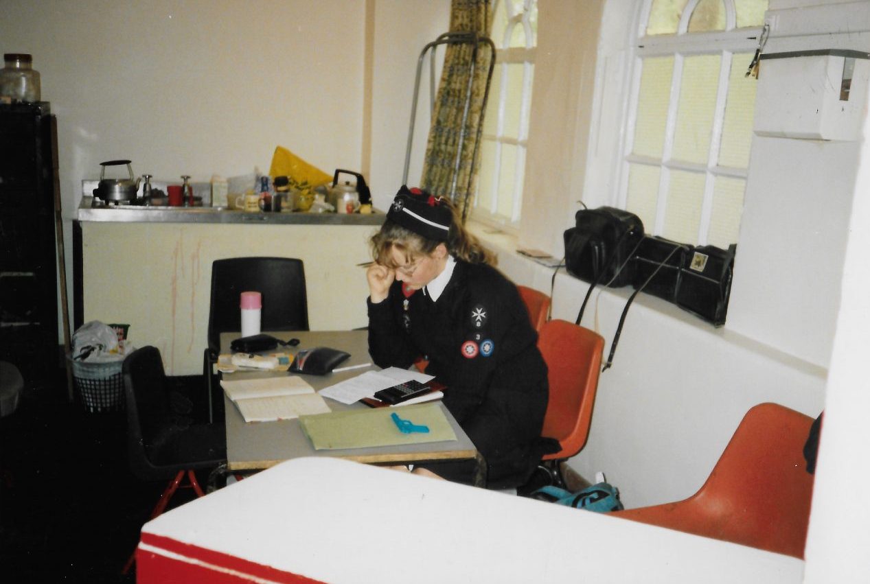 Colour photograph of a Cadet in black and whute uniform seated at a table in a kitchen, studying notes