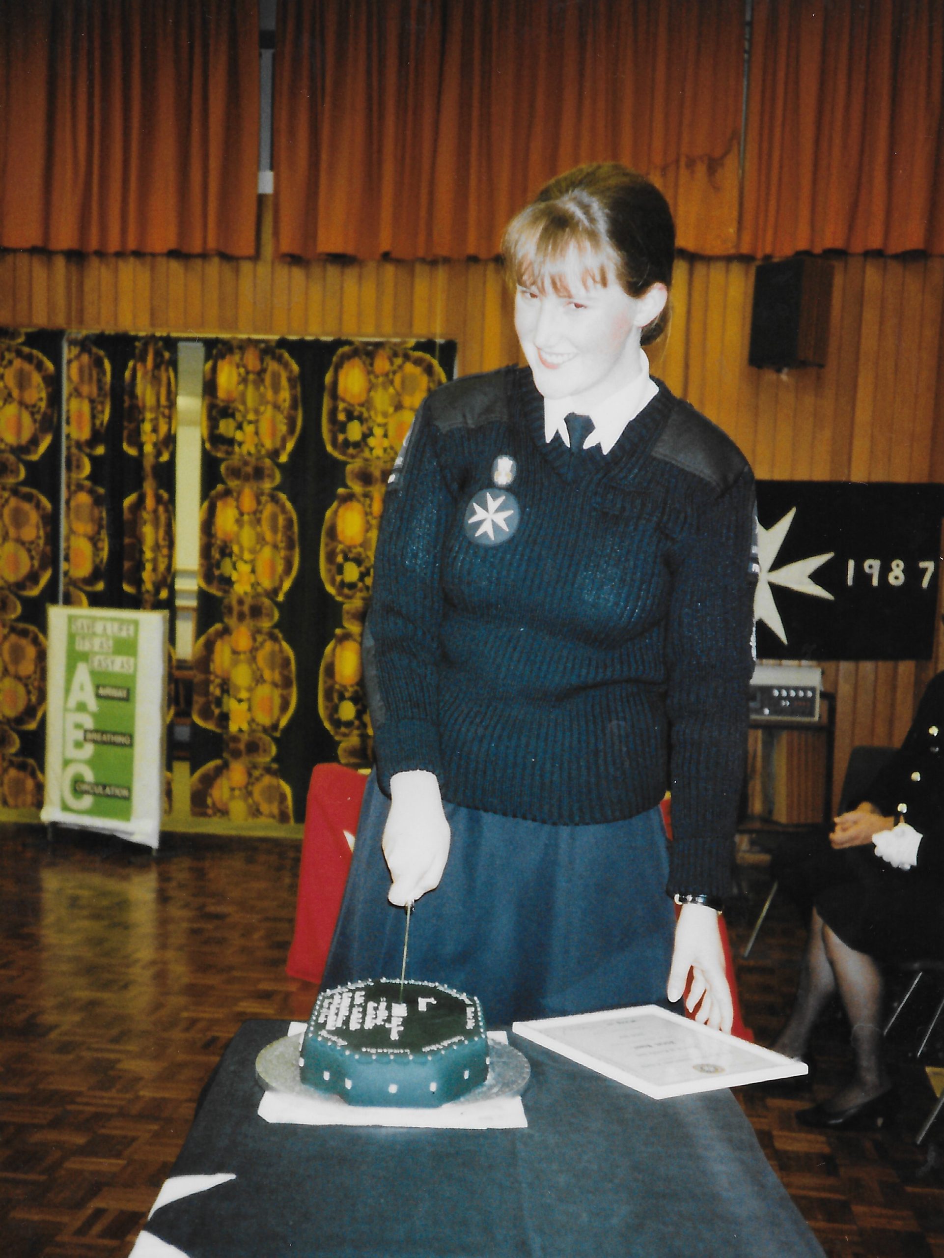 Colour photograph of a female Cadet in black and white uniform cutting into a cake, with her hand resting on her certificate