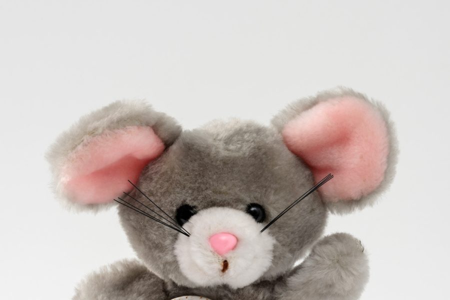 Colour photograph of a grey cuddly toy mouse with pink ears and black whiskers. It wears a badge reading 'I was at the Great St John Party' 1987'.