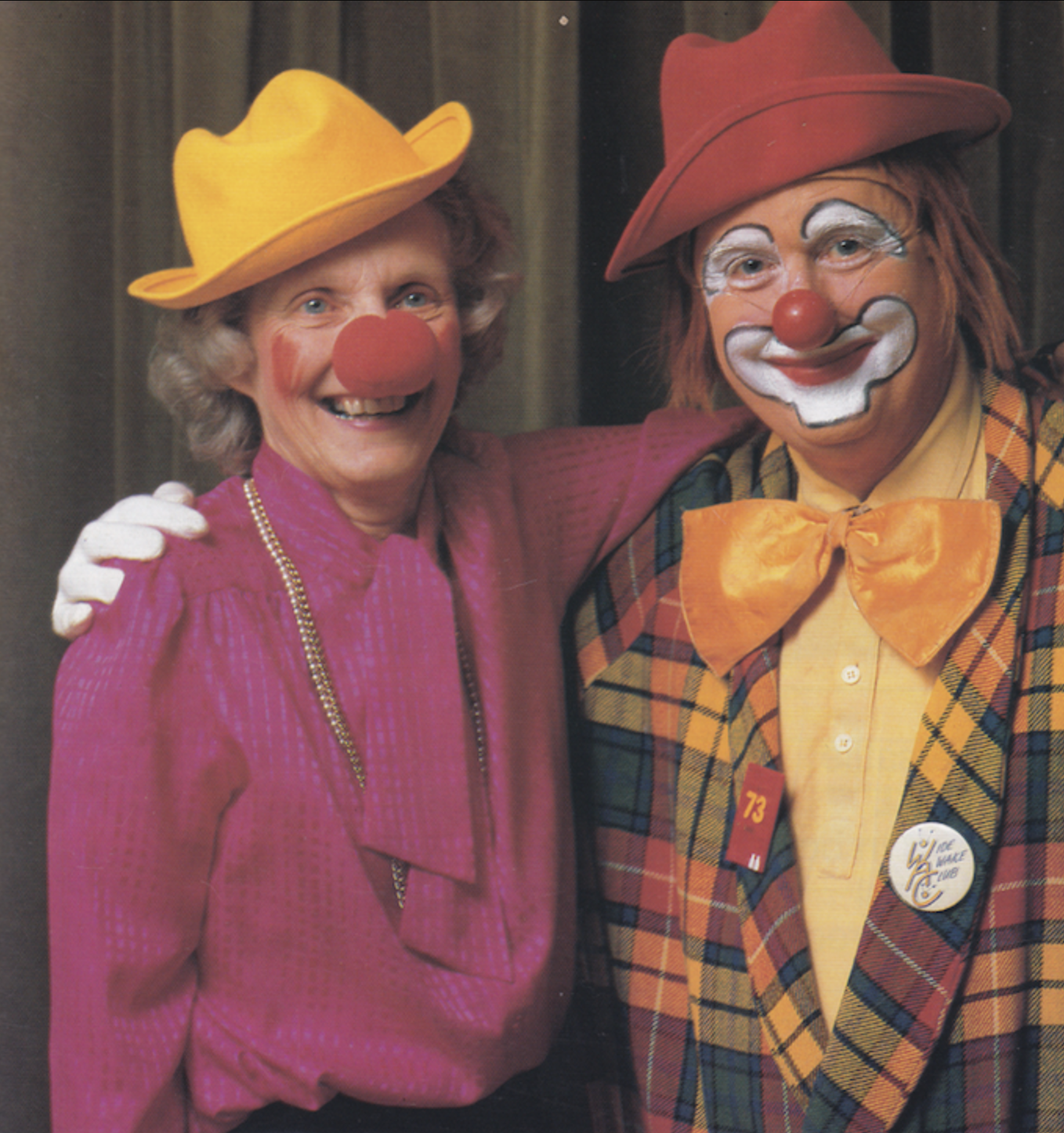 Colour photograph of a man and woman. The man on the right is dressed as a clown. The woman on the left is wearing a foam red nose.